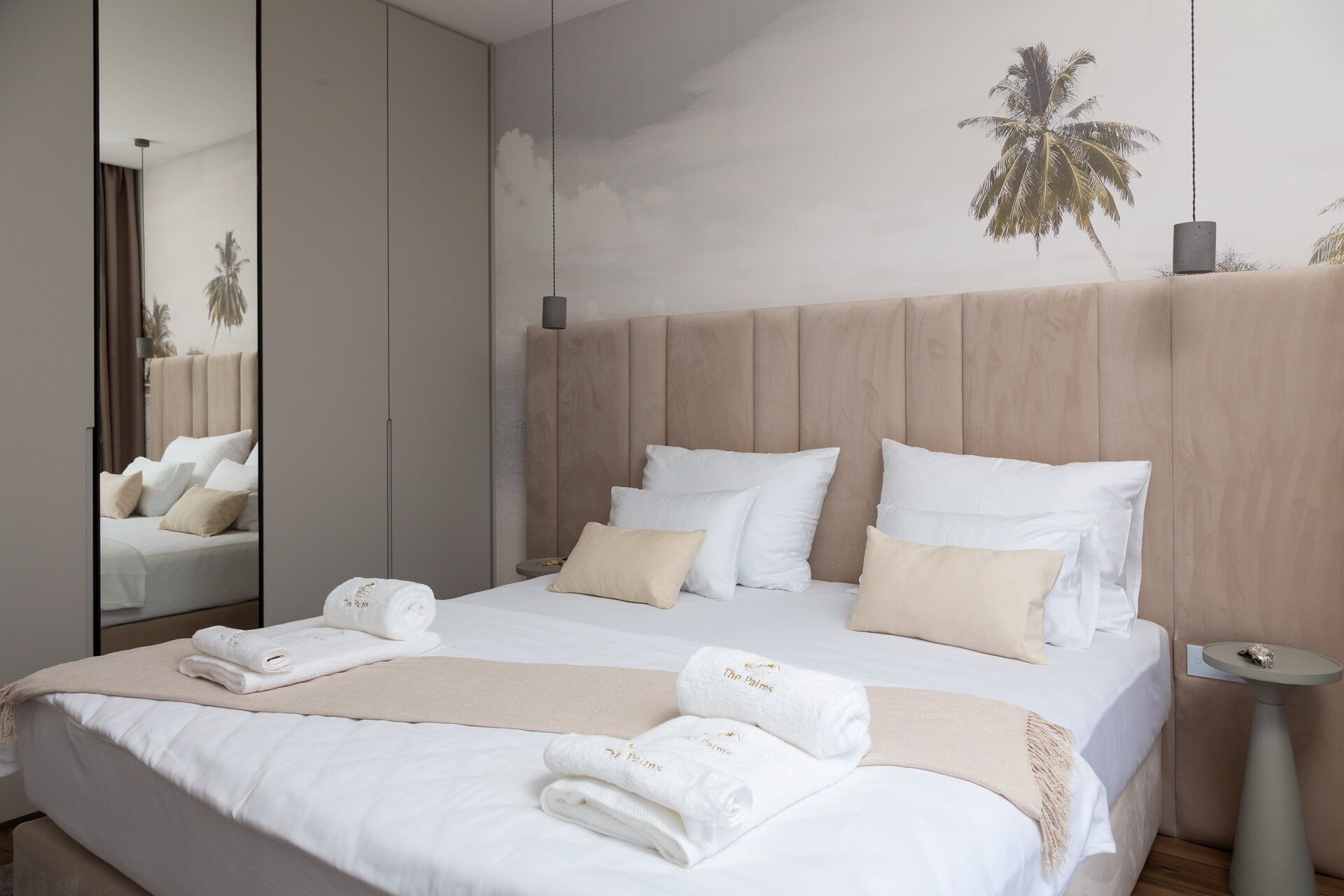 Een hotelkamer met een groot bed, een spiegel en een muur met een palmbomen muurschildering.