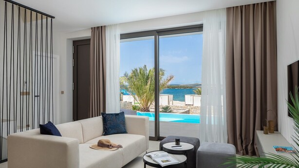 Habitación de hotel moderna con un gran ventanal que ofrece vistas a una piscina y al mar.