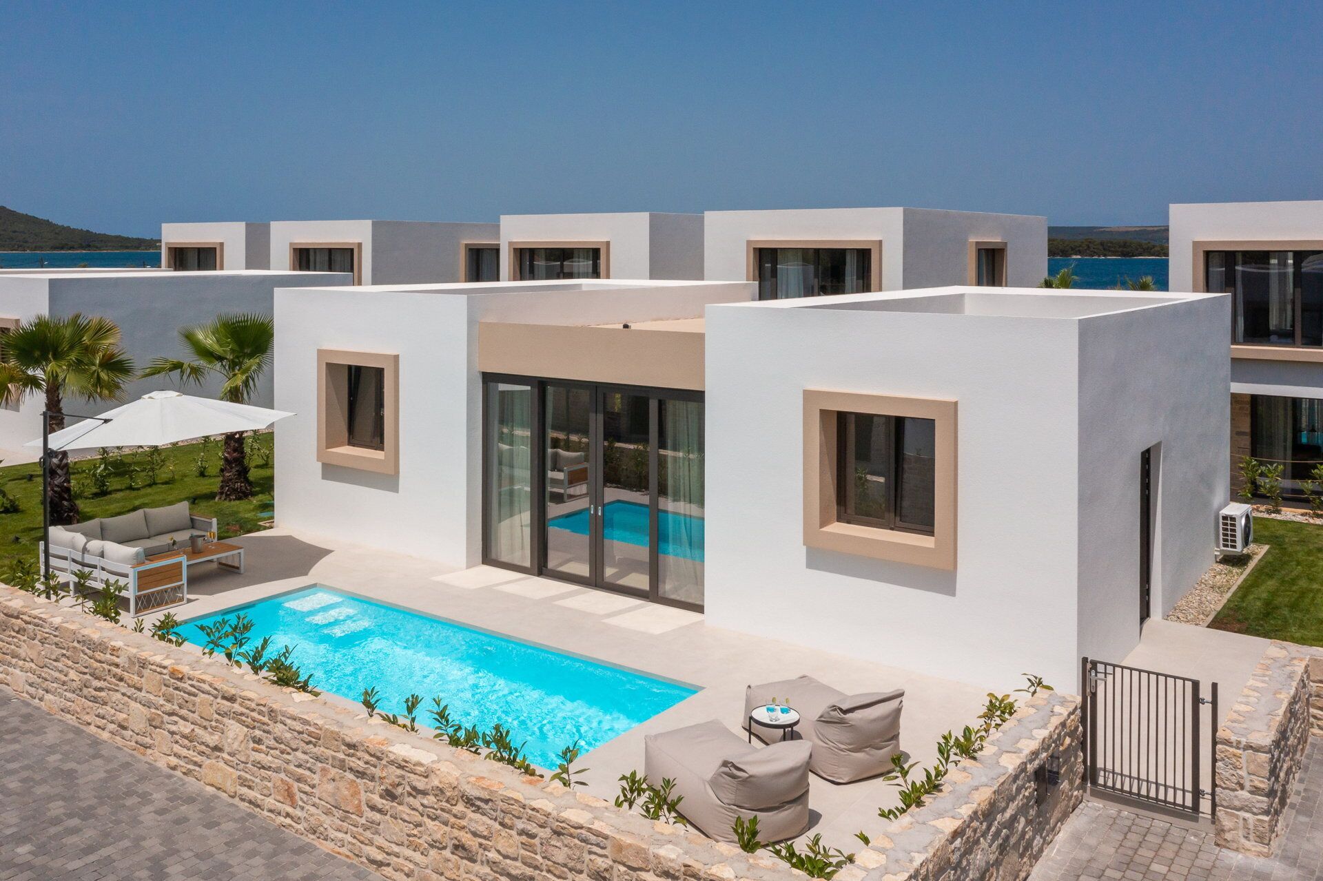 A modern building with a swimming pool, outdoor seating, and a view of the sea.