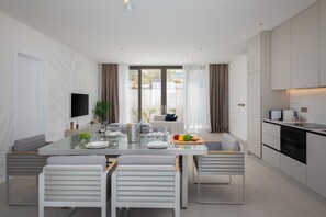 A modern kitchen with a dining area, featuring a large table with chairs, a TV mounted on the wall, and a view of the outdoors through the windows. - The Palms Resort - Villa Dream IV (Tkon)