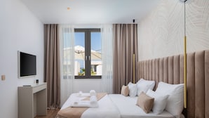 A modern hotel room with a large bed, a bedside table, a television, and a window with curtains. - The Palms Resort - Villa Dream IV (Tkon)