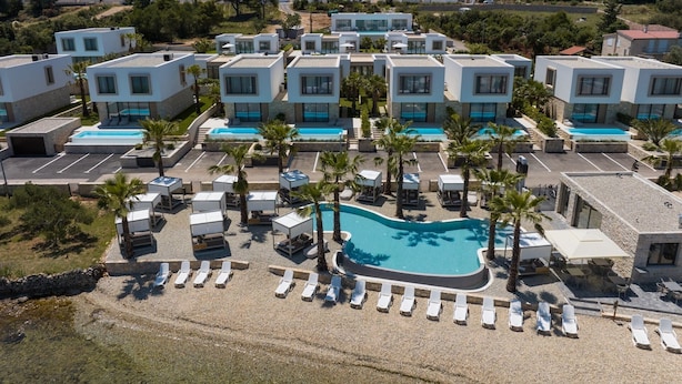 Een modern resort met meerdere witte gebouwen, een centraal gelegen zwembad en palmbomen.