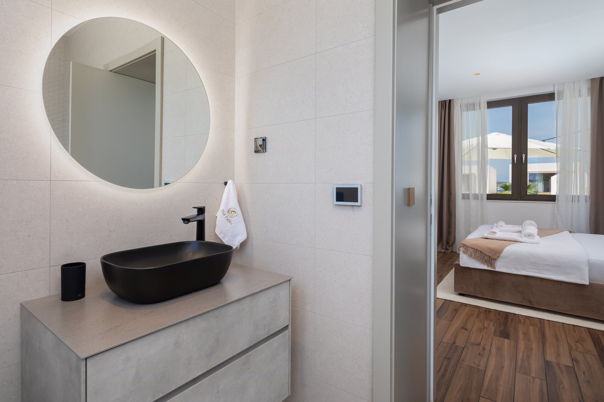 A modern bathroom with a round mirror, a black vessel sink, and a towel hanging on the wall.