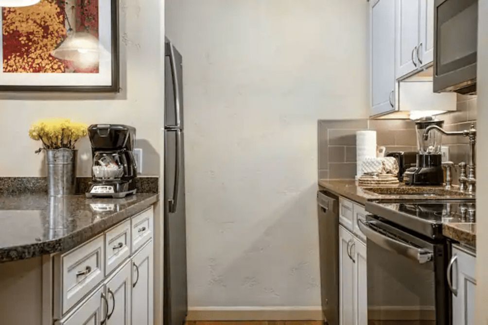 A modern kitchen with white cabinets, a stainless steel refrigerator, a coffee maker, and a microwave.