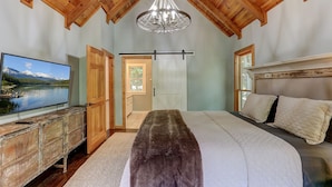 Quarto com uma cama grande, uma televisão sobre uma cômoda de madeira e um candelabro.