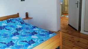 A bedroom with a wooden bed, a blue floral bedspread, a hanging light fixture, and a small bedside table with a lamp. - Town house in the heart of a typical Lot village (Saint-Sozy)