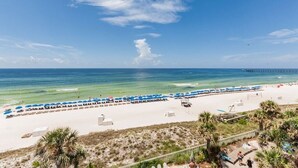 Ein Strand mit Reihen blauer Sonnenschirme und Liegestühle, ein sandiger Uferstreifen und ein klarer, blauer Himmel.