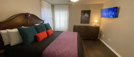 A bedroom with a bed, a ceiling fan, a dresser, a TV, and a window with curtains.