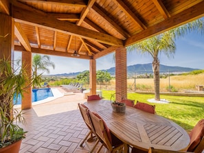 A covered outdoor area with a pool, lounge chairs, and a table with chairs.