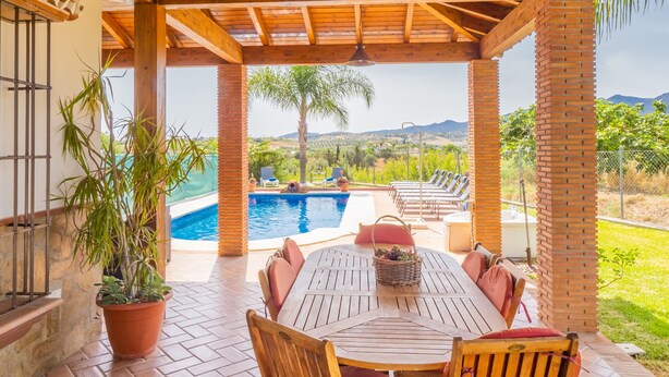 Un espace extérieur abrité, doté d’une piscine, de mobilier en bois et offrant une vue sur le paysage.