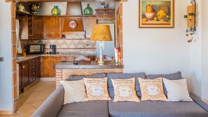 Un salon chaleureux avec un canapé, des coussins, un coin cuisine doté de meubles en bois, un four à micro-ondes et un tableau accroché au mur.