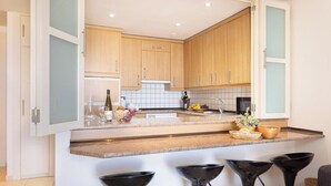 Eine moderne Küche mit Holzausbau, einer Granit Arbeitsplatte und vier schwarzen Barhocker.