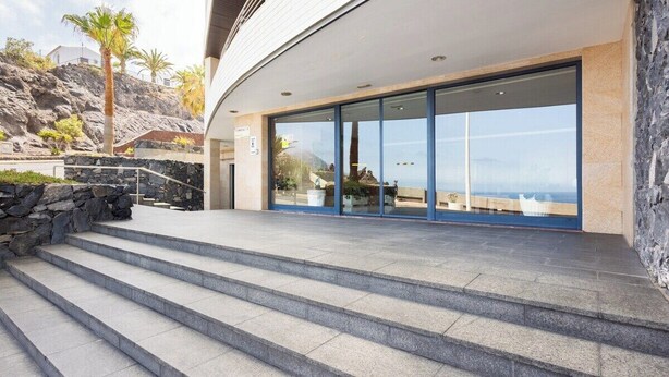 Ein modernes Gebäude mit Natursteinfassade, großen Glasfenstern und Blick auf das Meer.
