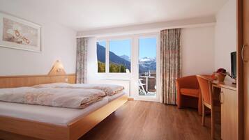 Une chambre à coucher avec un lit, un bureau, une chaise et une vue sur les montagnes par la fenêtre.