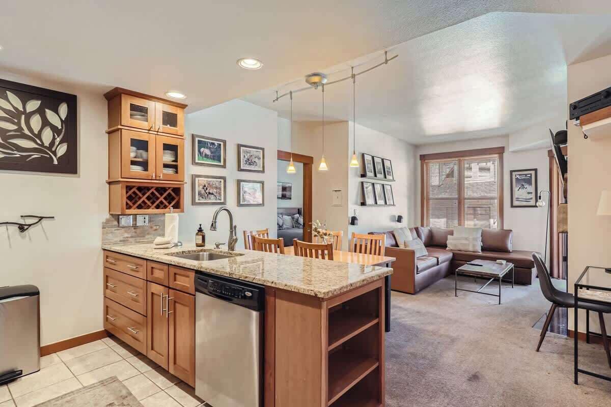 Cocina compacta con muebles de madera, lavavajillas y encimera de granito.