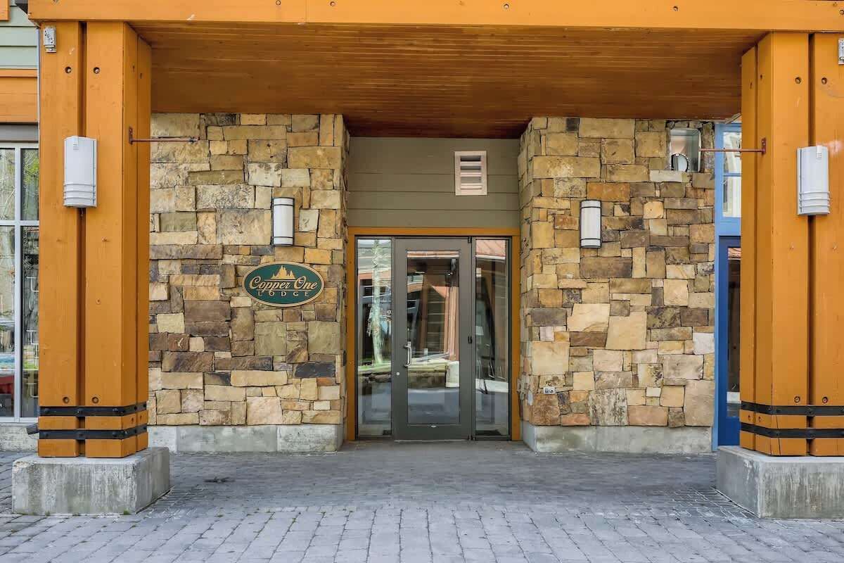 Entrada de un hotel con fachada de piedra, puerta de cristal y un letrero que dice 'Copper One'.