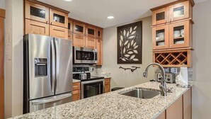 A kitchen with granite countertops, stainless steel appliances, wooden cabinets, and a decorative wall piece.