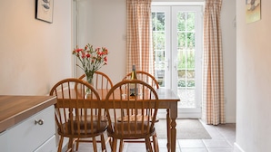A dining area with a wooden table and chairs, a vase with flowers, and a hanging light fixture.