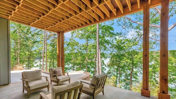 A covered outdoor seating area with wooden furniture and a view of a forested landscape.