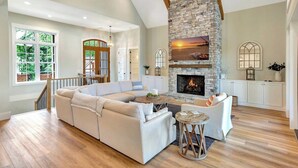 A spacious living room with a stone fireplace, a large sectional sofa, and a dining area with a wooden table.