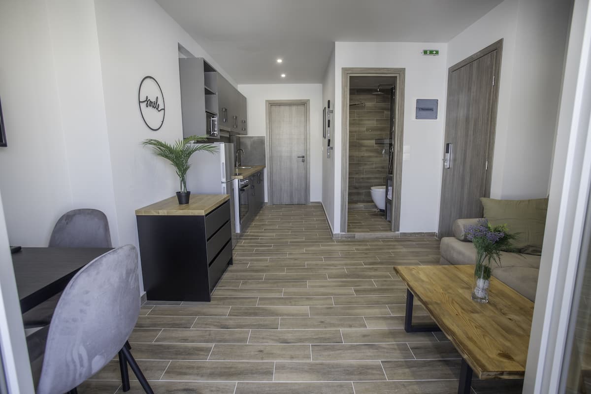 Une chambre d’hôtel moderne dotée d’une kitchenette, d’un coin repas avec une table et des chaises, d’un canapé et d’une table basse en bois.