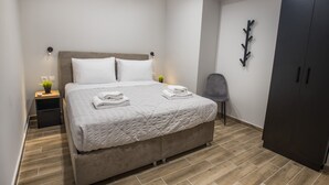 Un lit bien fait, recouvert d’une courtepointe, une table de chevet avec une lampe et une armoire dans une chambre moderne au plancher en bois.