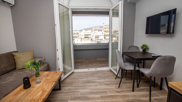Un balcon doté d’un plancher en bois, d’un canapé, d’une table avec un vase et un appareil photo, ainsi qu’un coin repas avec des chaises et un téléviseur.