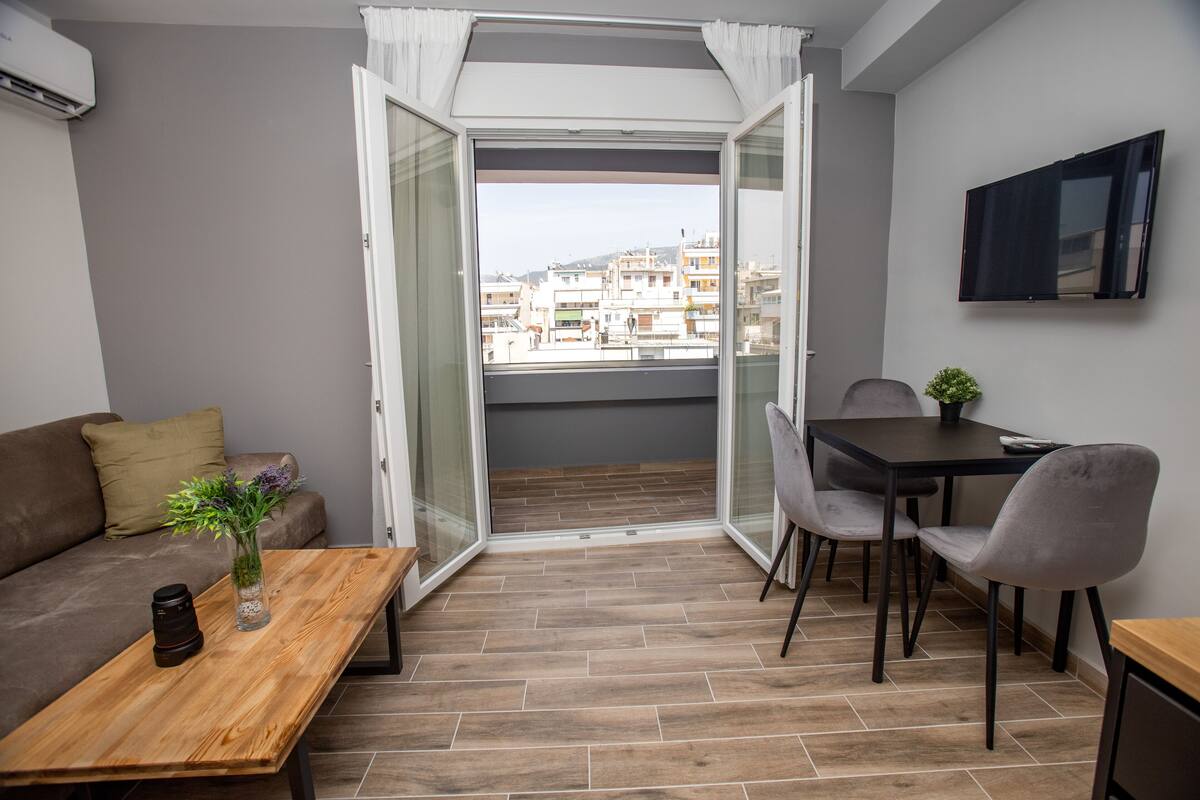Un balcon doté d’un plancher en bois, d’un canapé, d’une table avec un vase et un appareil photo, ainsi qu’un coin repas avec des chaises et un téléviseur.
