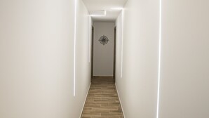 Un couloir moderne avec un plancher en bois et des murs blancs, agrémenté d’un luminaire au design géométrique au plafond.