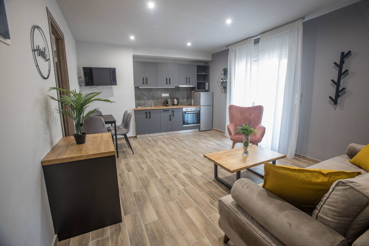 Un salon moderne avec un canapé, une table basse et un coin repas, la cuisine étant visible au fond.