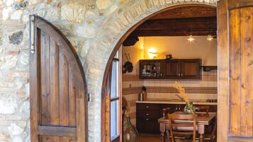 Un arco in pietra conduce a una cucina rustica con armadietti in legno e un tavolo da pranzo.