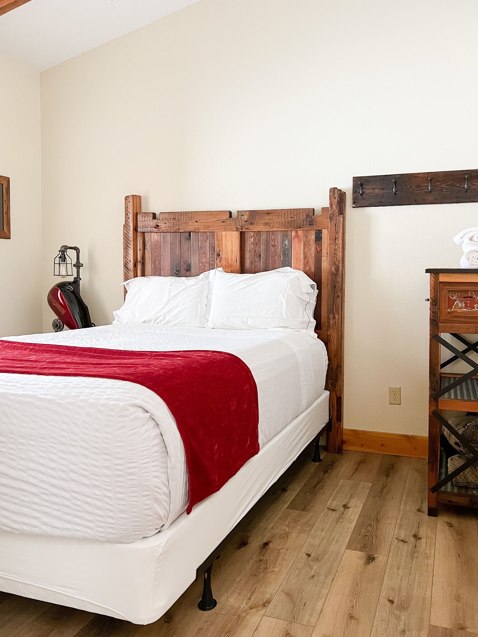 A bed with a wooden headboard, white bedding, and a red throw blanket.