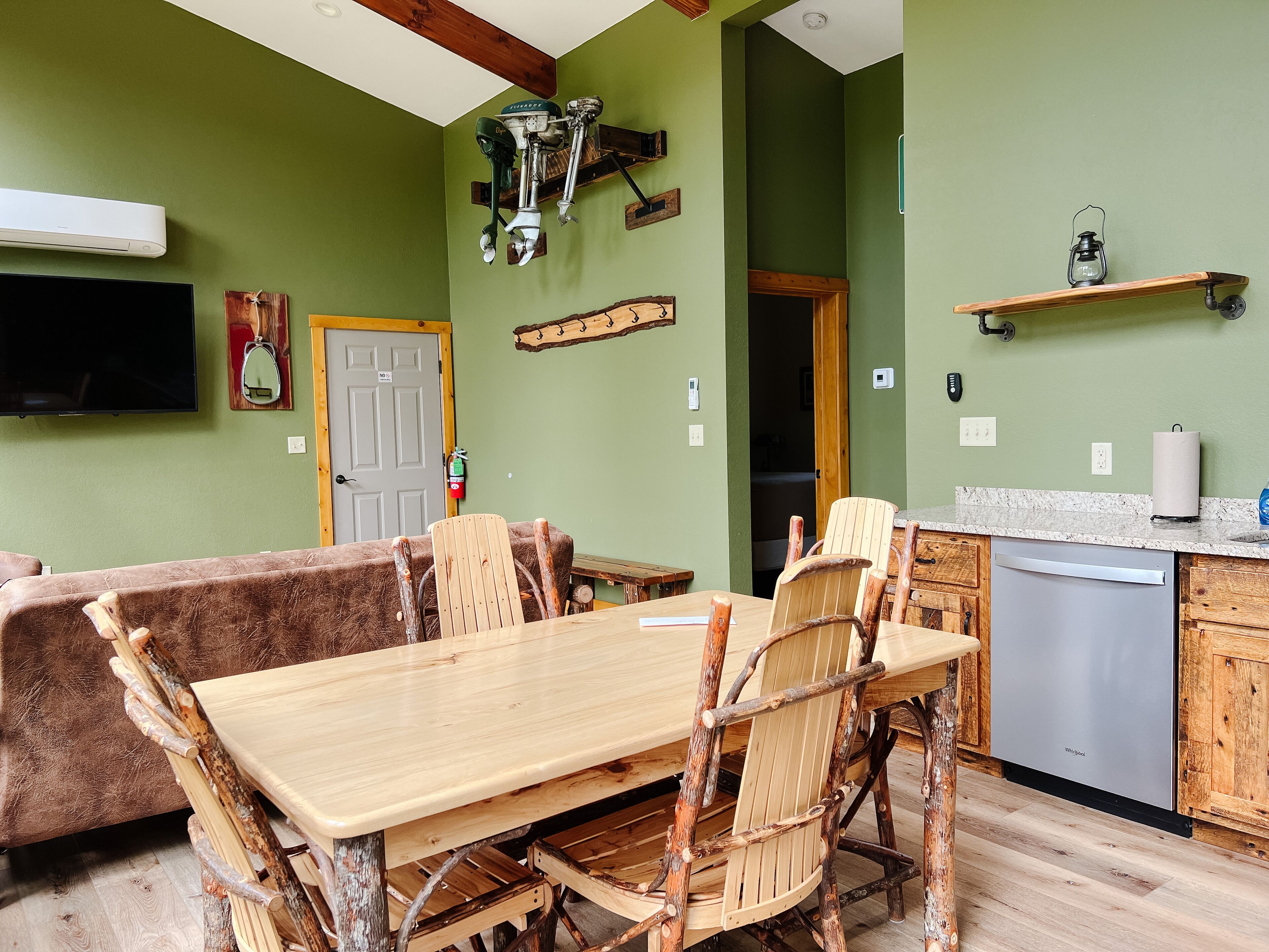 Een landelijke keuken met een houten tafel en stoelen, een inbouwvaatwasser en een groene wand.