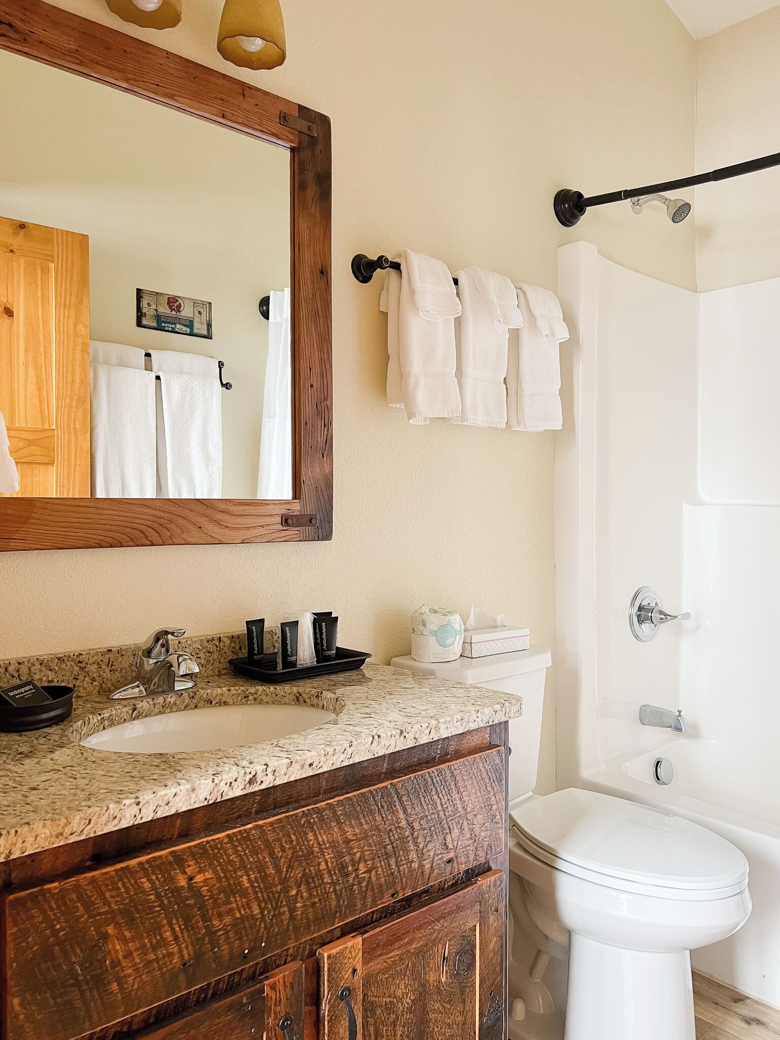 Un baño con tocador de madera, lavabo, espejo, inodoro y zona de ducha.
