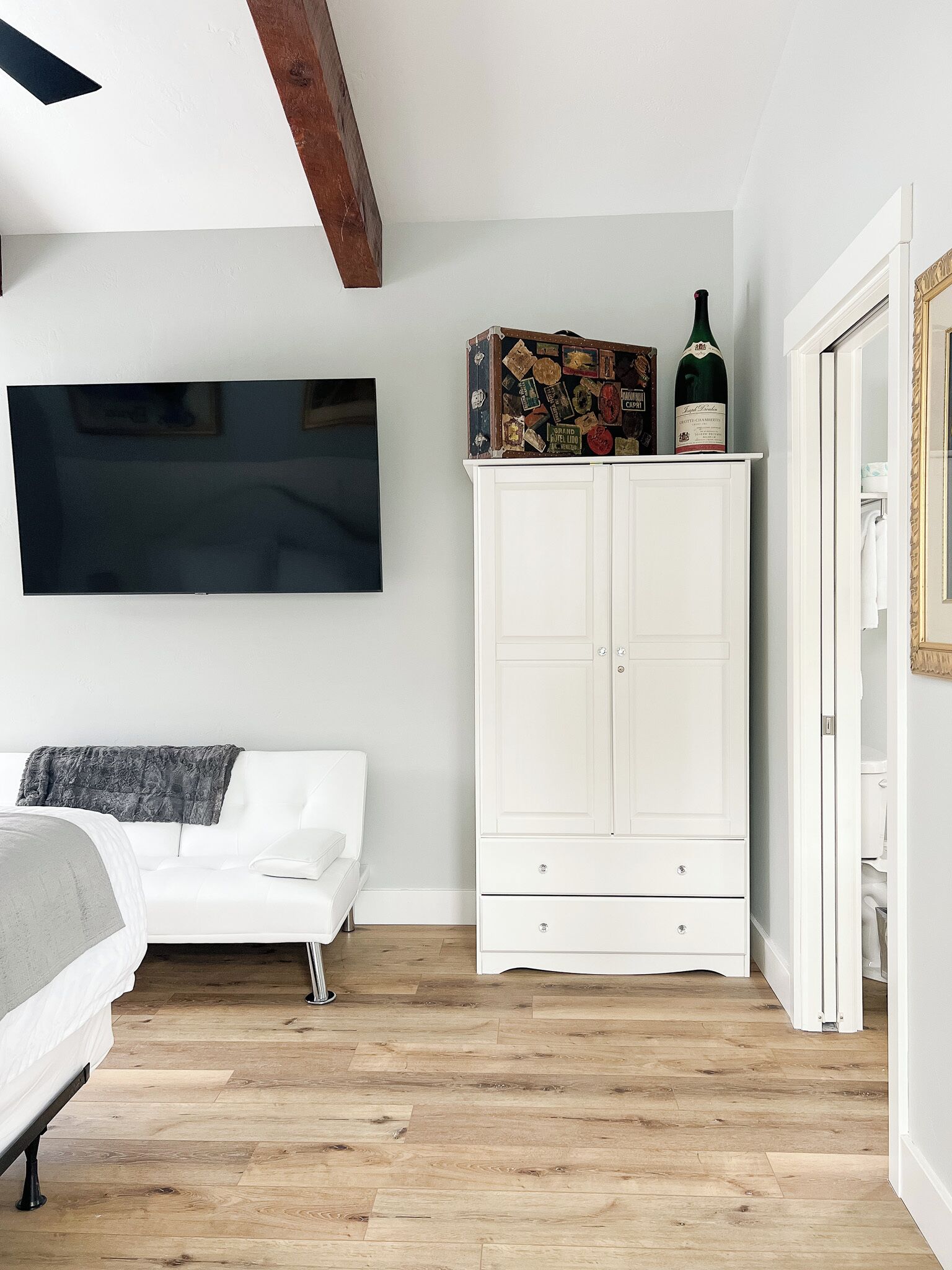 Un dormitorio con un armario blanco, una cama, un televisor y suelo de madera.