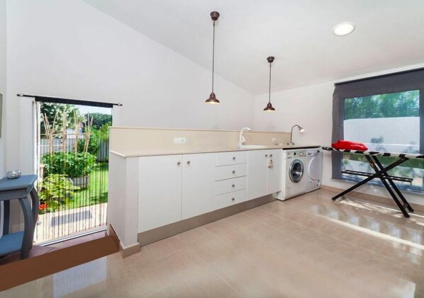 Une cuisine moderne avec des meubles blancs, un lave-linge et des luminaires suspendus.