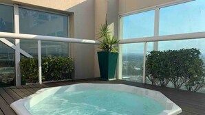 Een hottub op een houten terras met grote ramen en uitzicht over de stad.