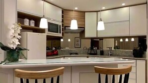 Een moderne keuken met witte kasten, een centraal eiland met twee houten barkrukken, hanglampen en een potorkidee.