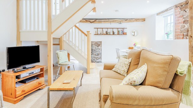 Ein Wohnzimmer mit einer Holztreppe, einem Flachbildfernseher, einem Sofa und einem Couchtisch.