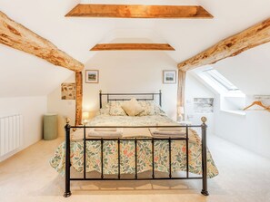 A bedroom with a bed, wooden beams, a radiator, a lamp, and a window.