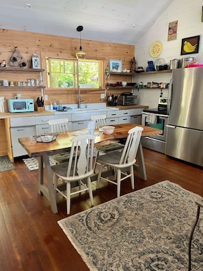 Une cuisine moderne avec des meubles en bois, un réfrigérateur en acier inoxydable et un coin repas comprenant une table et des chaises en bois.