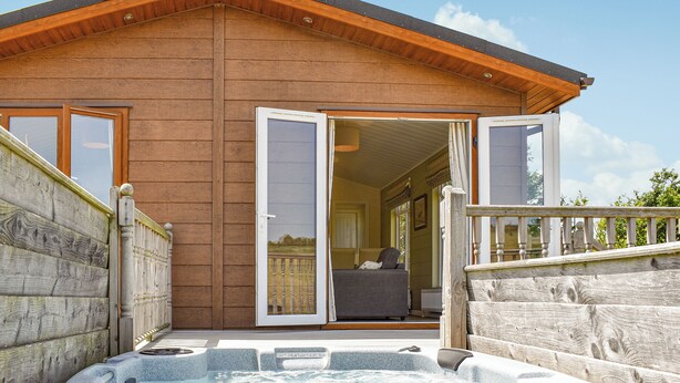 Eine Holzhütte mit Whirlpool, Balkon und einer Schiebetür zu einem Innenraum.