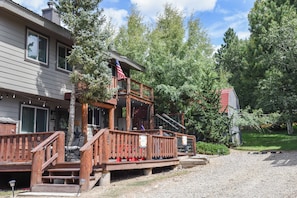 Une maison à deux étages avec une terrasse en bois, un porche avec des chaises et un drapeau américain.