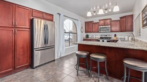 A modern kitchen with stainless steel appliances, wooden cabinets, and a large island with bar stools. - Your Home Away! Offering free heated pool ! Close to almost everything! (Chandler)