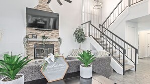 A modern living room with a fireplace, a staircase, and a welcome sign. - Your Home Away! Offering free heated pool ! Close to almost everything! (Chandler)