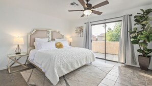 A bedroom with a bed, a ceiling fan, a nightstand, a lamp, a large potted plant, and a sliding glass door leading to a balcony. - Your Home Away! Offering free heated pool ! Close to almost everything! (Chandler)