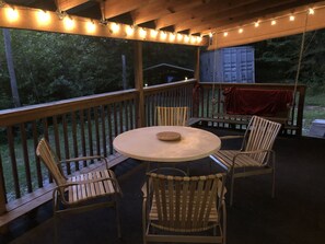 A covered outdoor seating area with a round table and four chairs, string lights, and a swing.
