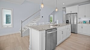 A modern kitchen with white cabinets, a stainless steel refrigerator, a dishwasher, and pendant lighting. - Modern Single Family Home 5 minute walk to the Beach! Linens Included! (Carolina Beach)