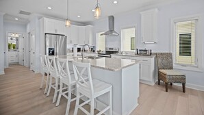 A modern kitchen with white cabinetry, a large island with bar stools, stainless steel appliances, and pendant lighting. - Modern Single Family Home 5 minute walk to the Beach! Linens Included! (Carolina Beach)