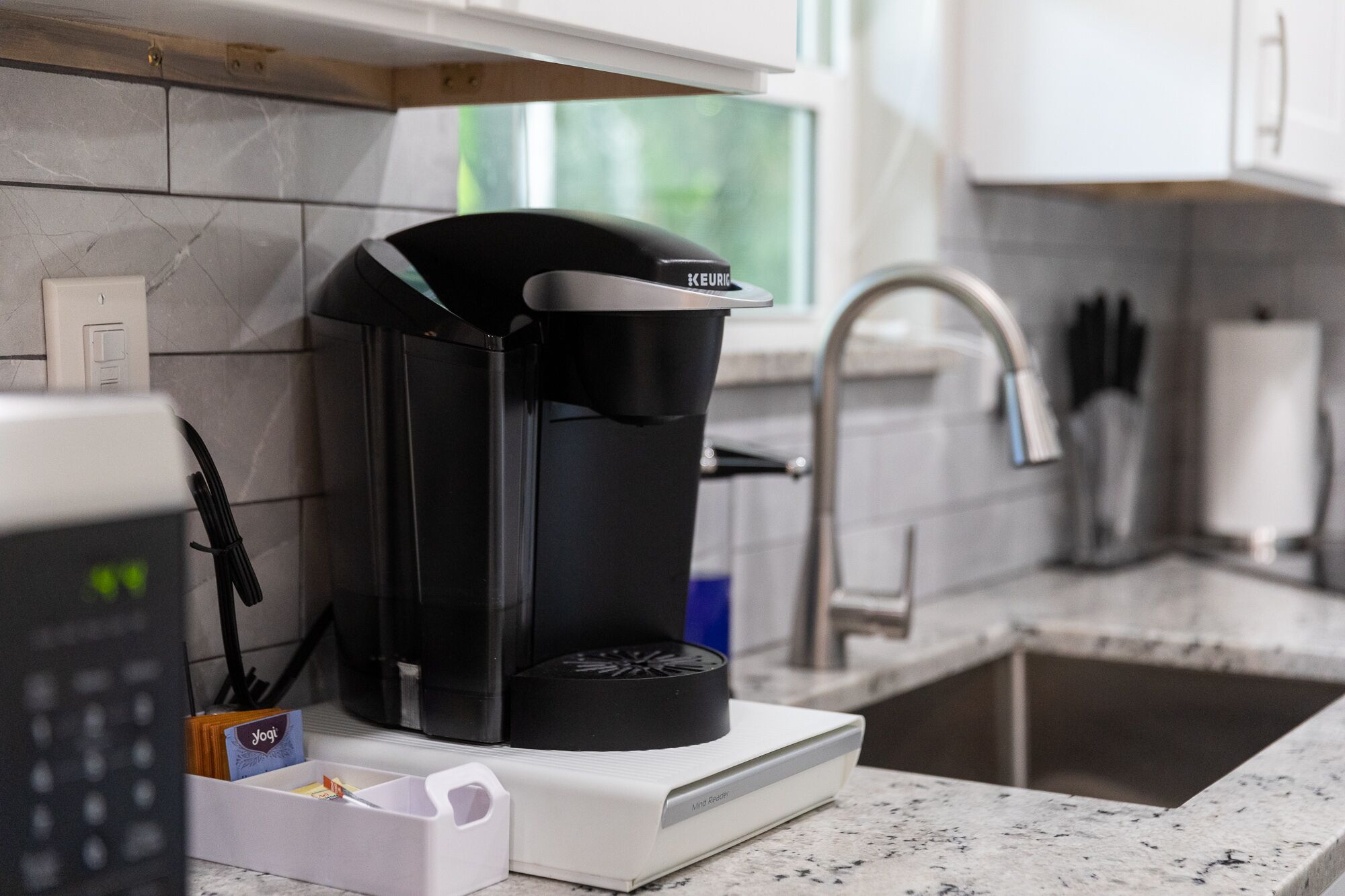 En kaffemaskine på en bordplade med en vask og et vindue i baggrunden.